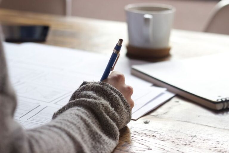 Quality Coffee - person writing on brown wooden table near white ceramic mug
