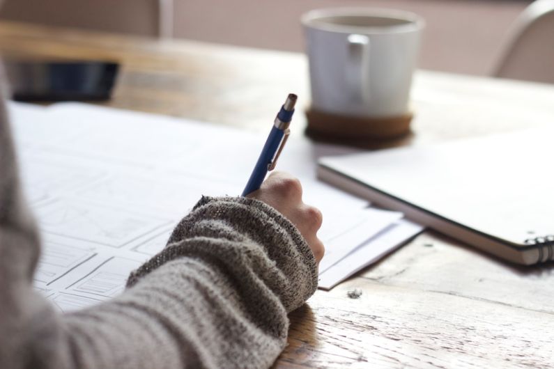 Quality Coffee - person writing on brown wooden table near white ceramic mug