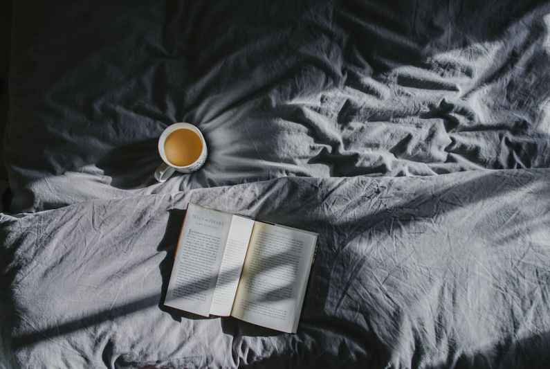 Coffee Rituals - white ceramic mug beside book on gray textile