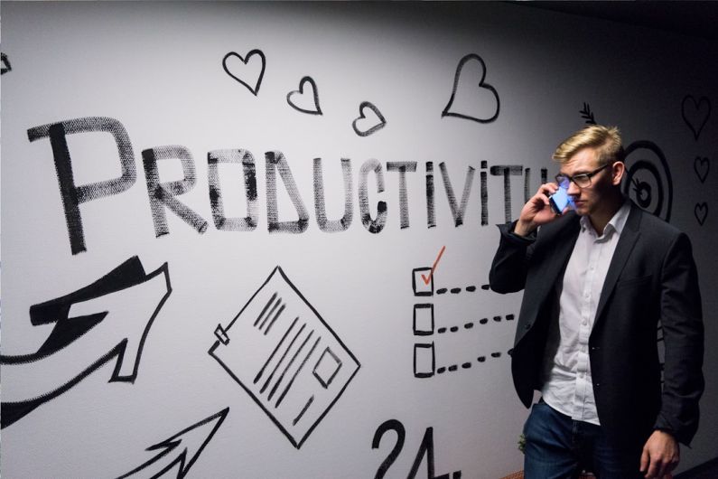 Productivity - man holding smartphone looking at productivity wall decor